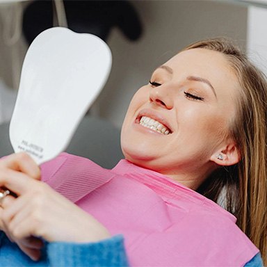 Woman in dentist’s chair looking at her teeth in a mirror